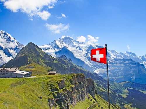 Paisaje montañoso con grandes picos nevados el fondo y la bandera de Suiza ondenado en primer plano