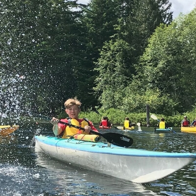 Joven salpicando con un remo subido a una canoa en un lago de Canadá