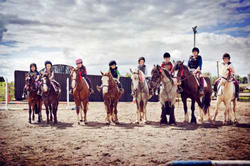 Niños y adolescentes con cascos de equitación en fila mirando a cámara subidos a ponis