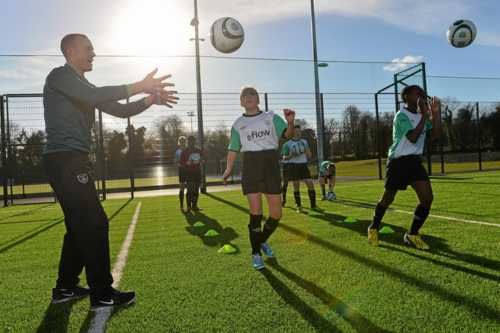 Chicos y chicas junto con su entrenador de fútbol realizando ejercicios de técnica