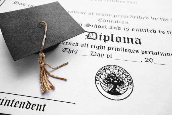 Fotografía de un gorro de graduación sobre un diploma de instituto escrito en inglés y sellado
