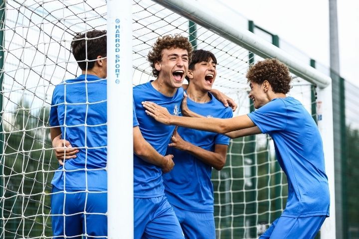 Chicos abrazándose con expresión alegre dentro de una portería con la equipación del Chelsea FC. Están realizando un campamento de fútbol con el chelsea en Inglaterra