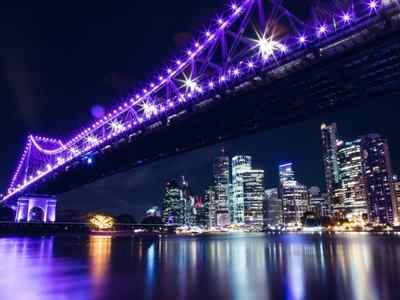 Skyline nocturno de Brisbane, Australia, con un puente iluminado en color violeta.