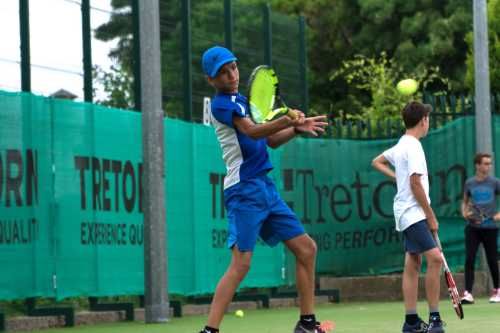 Chico con ropa azul y blanca agarrando una raqueta de tenis de color amarilla fosforita, jugando a tenis.